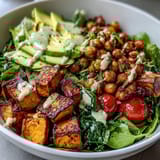 Savory roasted chickpeas and tender sweet potatoes nestled on a bed of greens, topped with cucumber, tomatoes, and avocado for a nourishing Breakfast Buddha Bowl.  