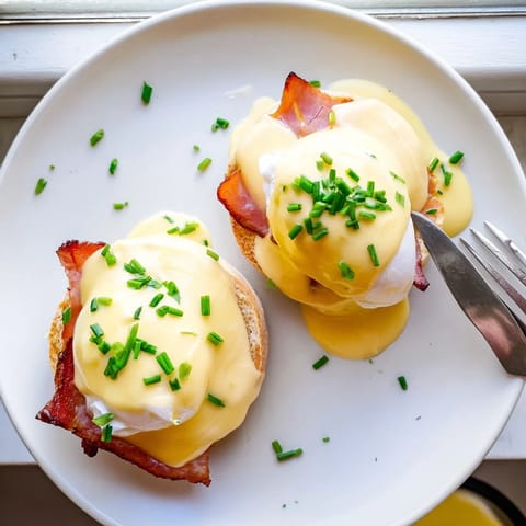 Classic brunch Eggs Benedict featuring runny poached egg yolks, Canadian bacon, and warm hollandaise on a crisp English muffin.