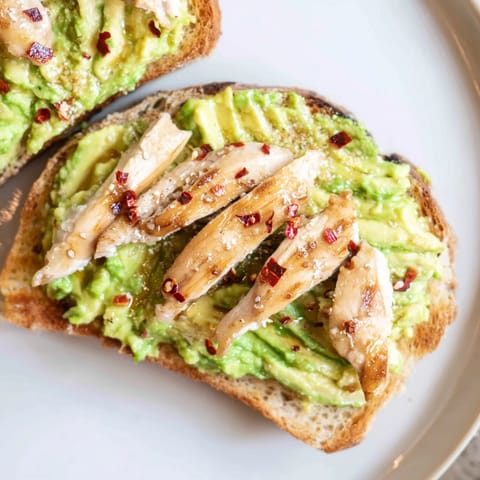 Creamy smashed avocado and grilled chicken slices top crispy sourdough toast, finished with chili flakes and honey for a savory-sweet kick.