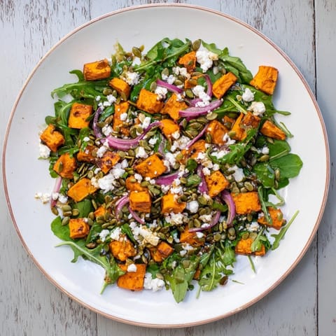 A close-up of the Roasted Sweet Potato Salad showing golden sweet potato cubes, red onion slices, and a glossy honey-lime dressing.