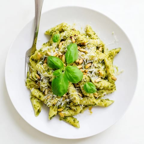 Creamy sunflower seed pesto pasta in a white bowl garnished with basil, showing a rich, vibrant green sauce coating the noodles.