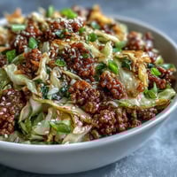 Steaming Egg Roll in a Bowl with ground pork, cabbage, carrots, and green onions in a skillet.  
