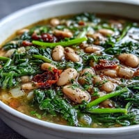 A steaming bowl of Tuscan white bean and spinach soup, brimming with tender beans and fresh greens in a savory broth.